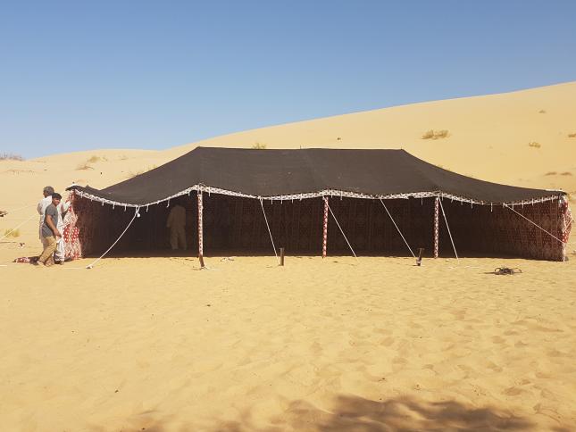 Dark traditional Bedouin tent pitched on sand beside desert dunes