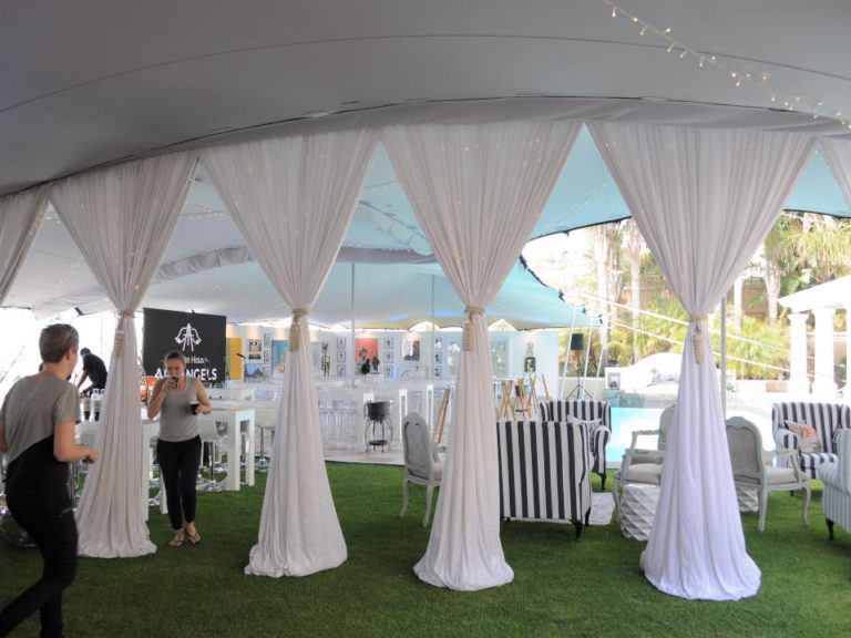 Entrée de la tente extensible avec des rideaux blancs froncés, des tables blanches et des invités