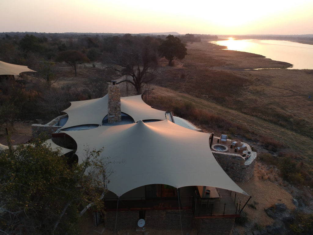 Aerial view of beigeLuxury Custom Glamper Stretch at a remote camp beside water at sunset in Zambia