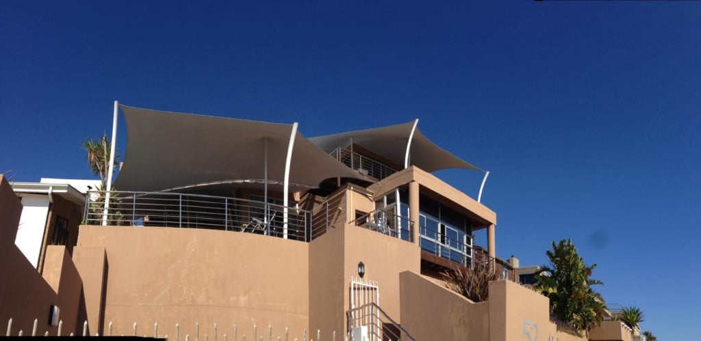 Beige bespoke stretch tent canopy shading a rooftop terrace on a coastal building for a residential area