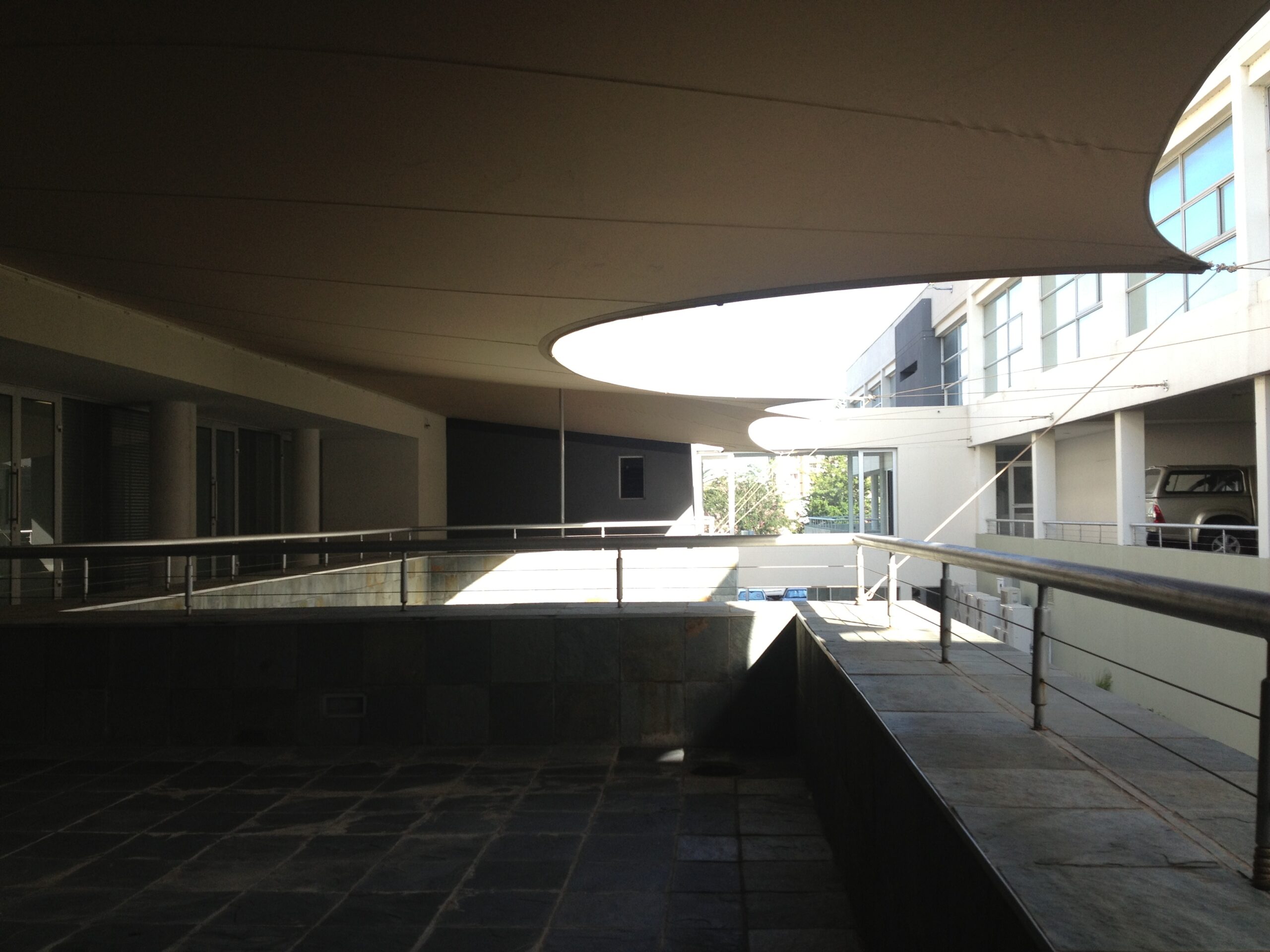 Beige Large Catenary Custom Stretch Tent covering a paved courtyard between modern buildings; located in Western Europe