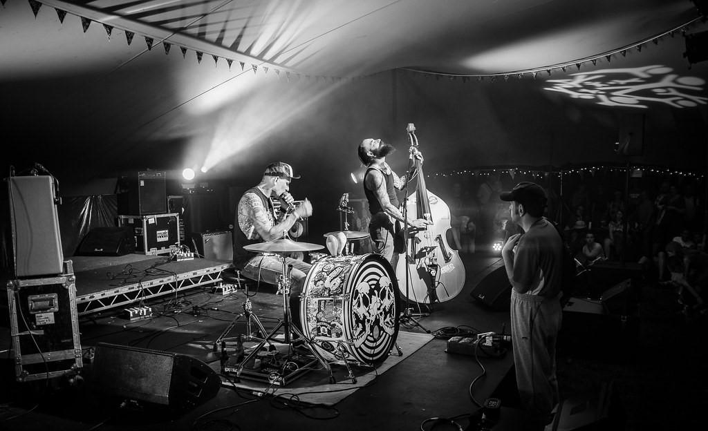 Zwart-witfoto van een band en een drumstel die optreden onder een stretchtent; genomen in het Verenigd Koninkrijk