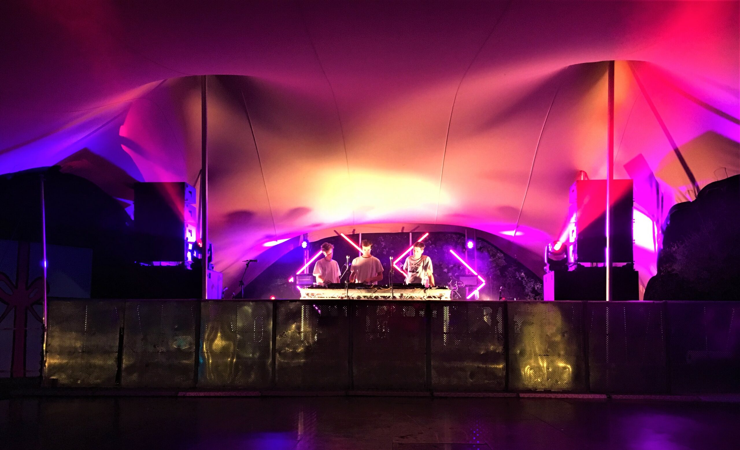 Festival stage beneath a Flextent in Germany, illuminated pink, purple and orange at night