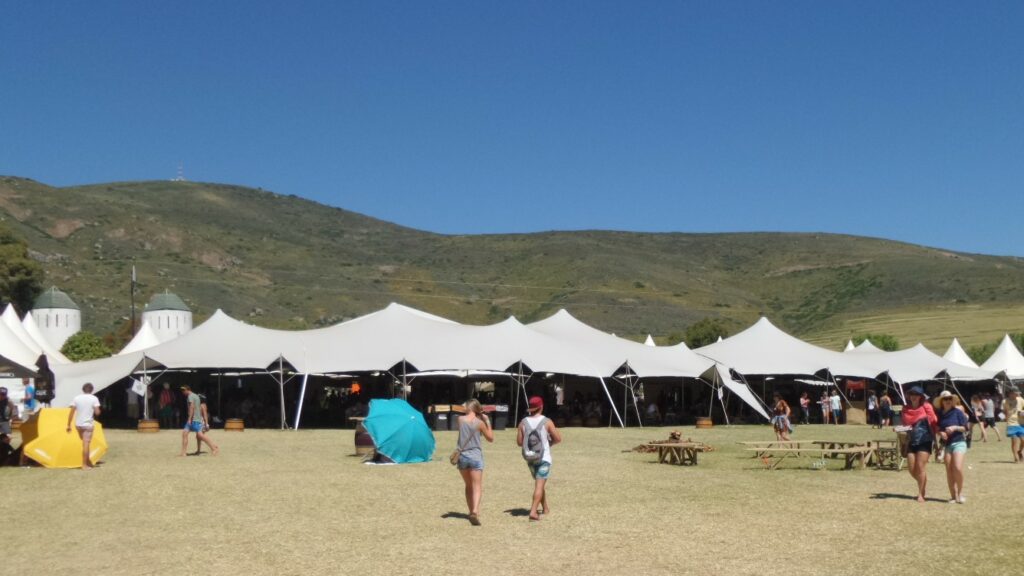 Aaneengesloten witte, grootschalige, modulair gekoppelde stretchtenten die een cateringruimte van een festival op een grasveld overspannen
