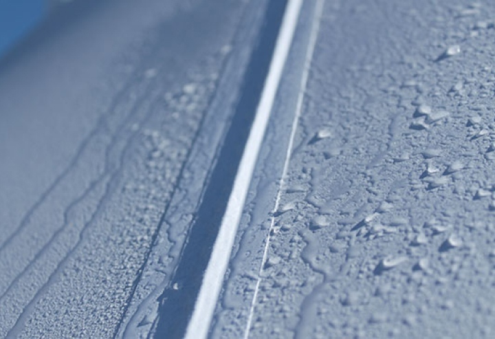 Gros plan sur une couture d'une toile de tente grise, avec des gouttelettes d'eau à la surface