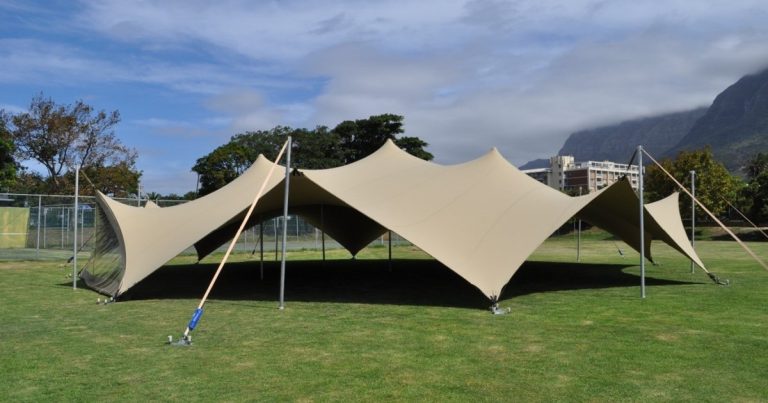 Beige stretch Arachnid tent met een diameter van 20 m op gras, met de bergen op de achtergrond