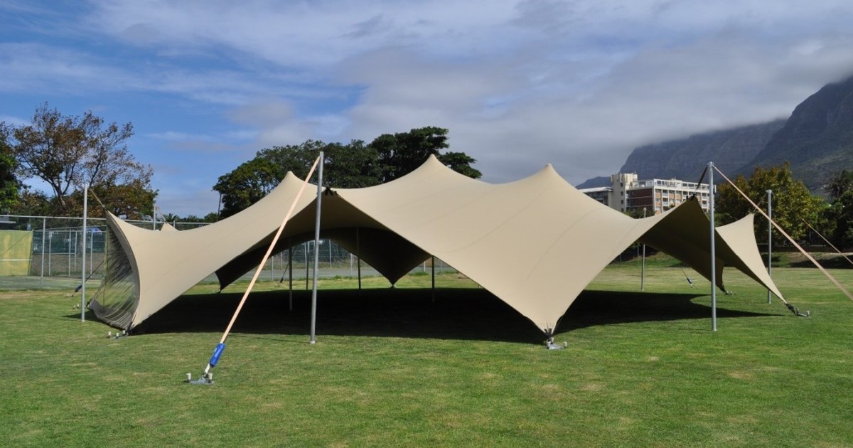 Beige 20m Diameter Arachnid stretch tent on grass with mountains behind it