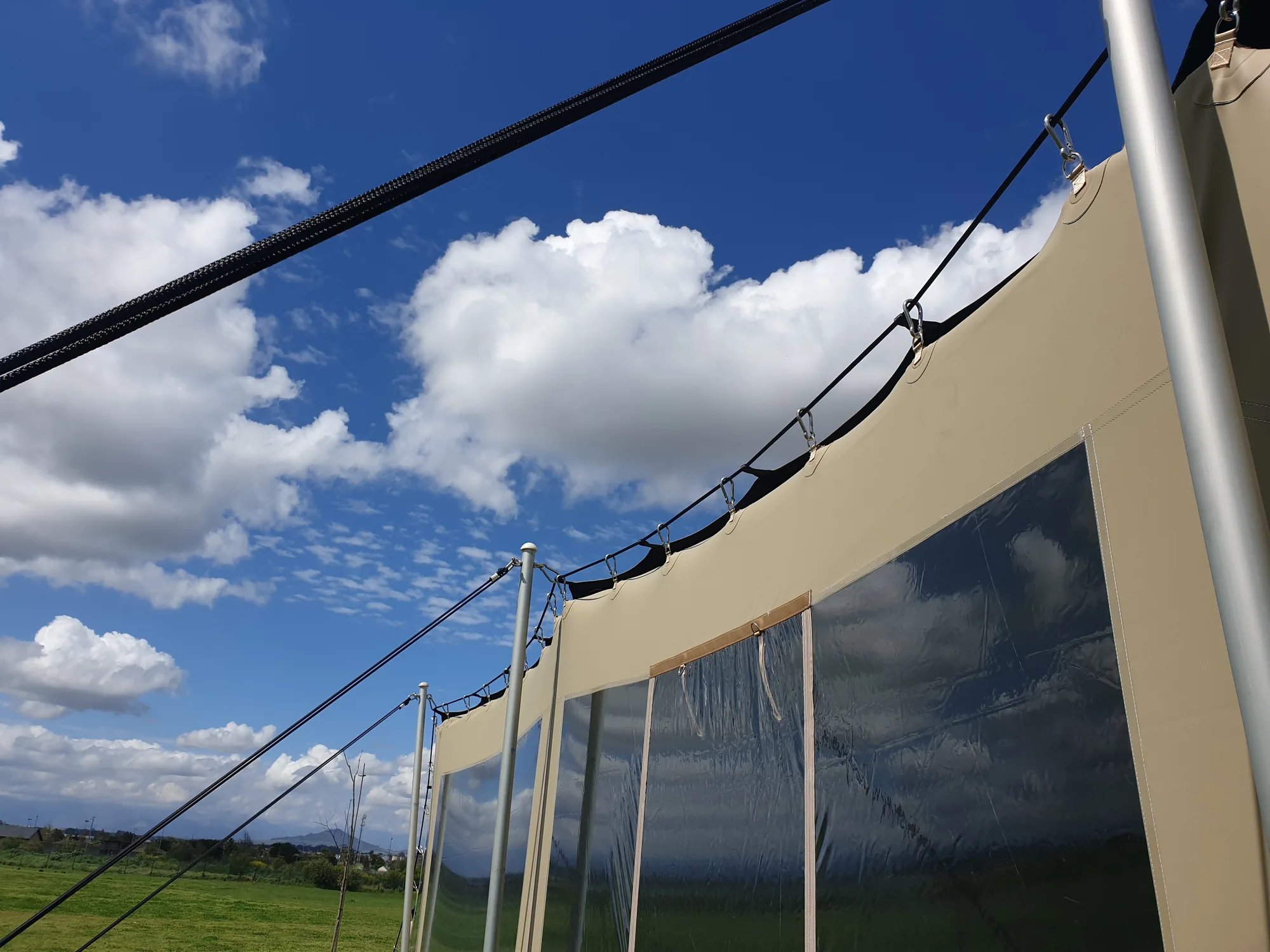 Clear wall panels with beige borders along the outside of a stretch tent in an open field