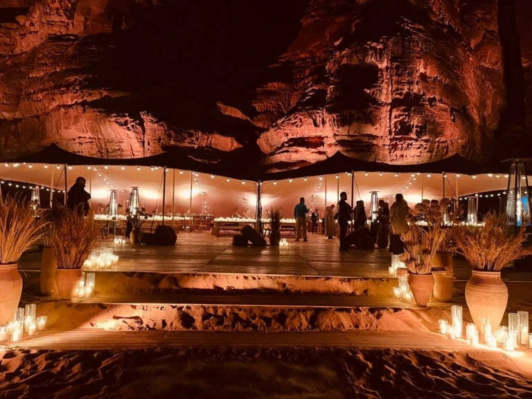 Illuminated desert hospitality stretch tents below rock formations at night — Linked Stretch Tents for AlUla Desert Polo, Saudi Arabia