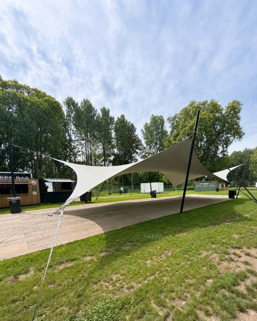 Light hypar stretch tent above a timber platform on a tree-lined lawn — 20 × 10 m Hypar Stretch Tent for a Festival in the Netherlands
