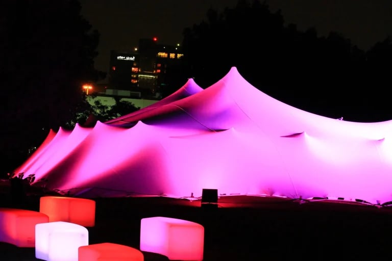 Vue extérieure de nuit, avec un éclairage rose, d'un grand complexe RHI tente stretch aménagé pour accueillir des événements d'entreprise au Moyen-Orient