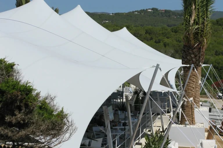 Vista estructural exterior de un sistema « Carpa Tensada » de RHI, de color blanco y fabricado a medida, integrado en un restaurante frente al mar