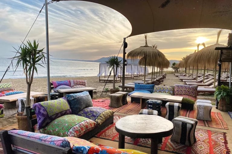Vista del salón al atardecer bajo el borde catenario de un sistema RHI Carpa Tensada a medida, integrado en un restaurante frente al mar