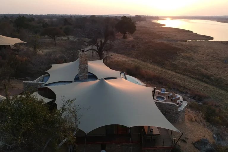 Vista aérea al atardecer junto al agua de un glamping personalizado de RHI Carpa Tensada integrado en un campamento ecológico apartado