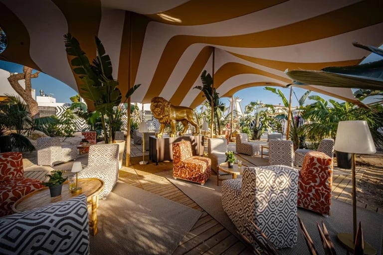 Vista del comedor bañado por la luz del sol, con una lona a medida a rayas de RHI Carpa Tensada que cubre la terraza amueblada de un restaurante en Europa