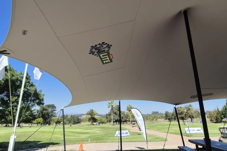 Vista a lo largo del borde catenario de una cubierta « Carpa Tensada » de RHI, fabricada a medida, que cubre la zona de gradas y de restauración de un campo de golf.