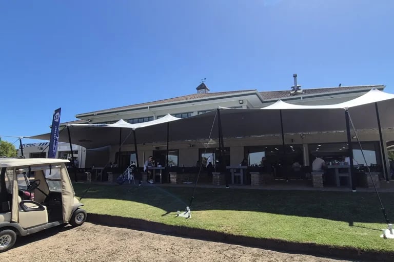 Amplia vista exterior del campo de golf desde una estructura « Carpa Tensada » de RHI, fabricada a medida, que cubre una zona de asientos y de recepción del campo de golf.