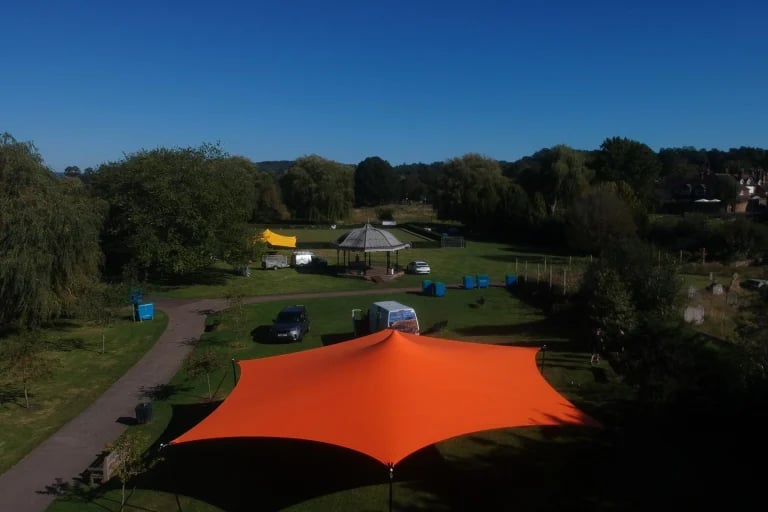 Vista aérea exterior de un gran sistema RHI Carpa Tensada de color naranja instalado en un jardín ajardinado