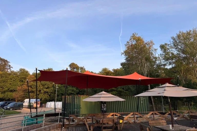 Vista desde el jardín de un gran RHI Carpa Tensada de color naranja que cubre una zona de descanso al aire libre