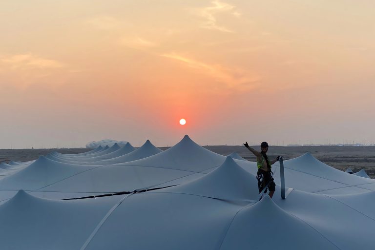 Vista desde la azotea al atardecer de un gran RHI Carpa Tensada sostenido por un sistema de vigas en un recinto para eventos situado en el desierto