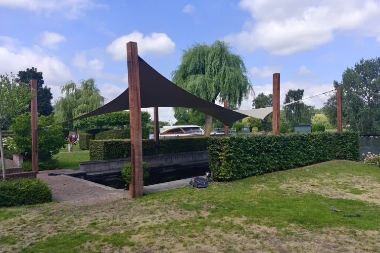 Vista estructural más detallada de una marquesina oscura a medida de RHI, sujeta entre postes de madera en un jardín ajardinado
