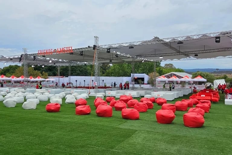 Vista general del público sentado en una amplia zona de eventos al aire libre con la marca, que cuenta con una estructura de trusses para el escenario, asientos e infraestructuras de hospitalidad.