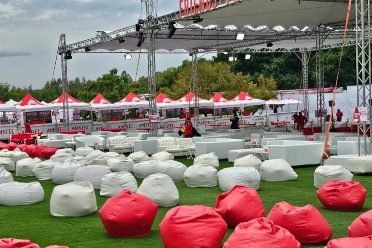 Vista desde los asientos situados junto al escenario de una amplia zona al aire libre dedicada a un evento de marca, con estructura de truss, asientos e infraestructura de hospitalidad