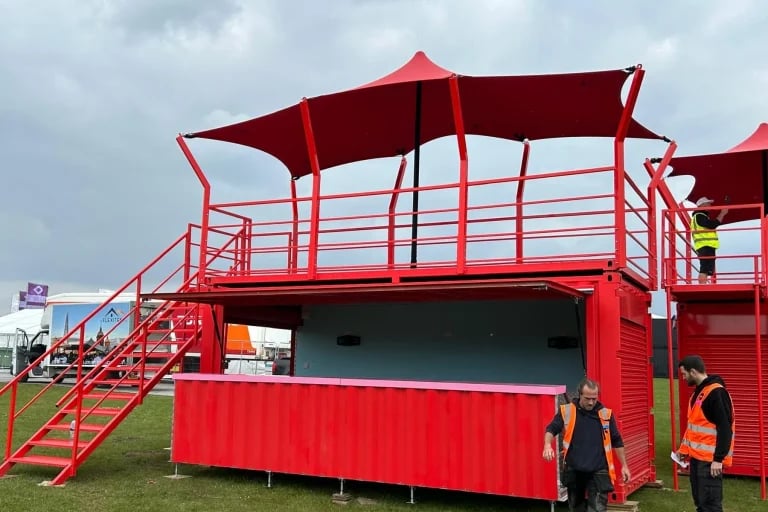 Vista exterior frontal de un local en un contenedor de color rojo con la marca, rematado con marquesinas personalizadas de RHI Carpa Tensada