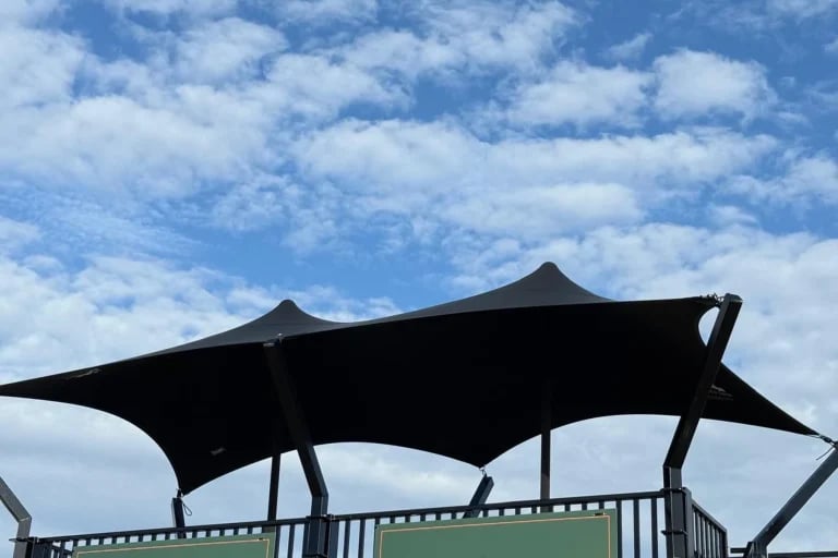 Vista exterior frontal de una marquesina « Carpa Tensada » de RHI, de color negro y fabricada a medida, instalada sobre una estructura de acogida construida con contenedores.