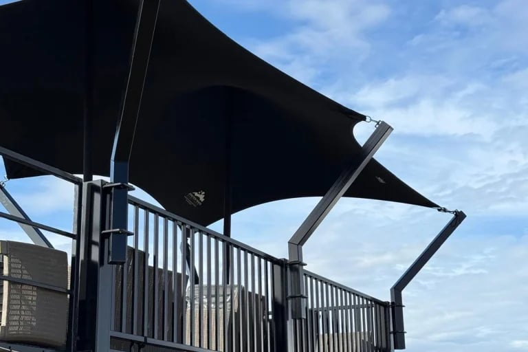 Vista lateral de la estructura de una marquesina negra personalizada de RHI Carpa Tensada instalada sobre una estructura de acogida en un contenedor