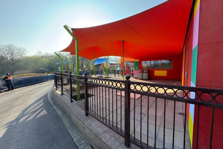 Vista desde la pasarela de una cubierta « Carpa Tensada » de RHI, fabricada a medida en color naranja brillante, que cubre una zona de asientos del parque Legoland