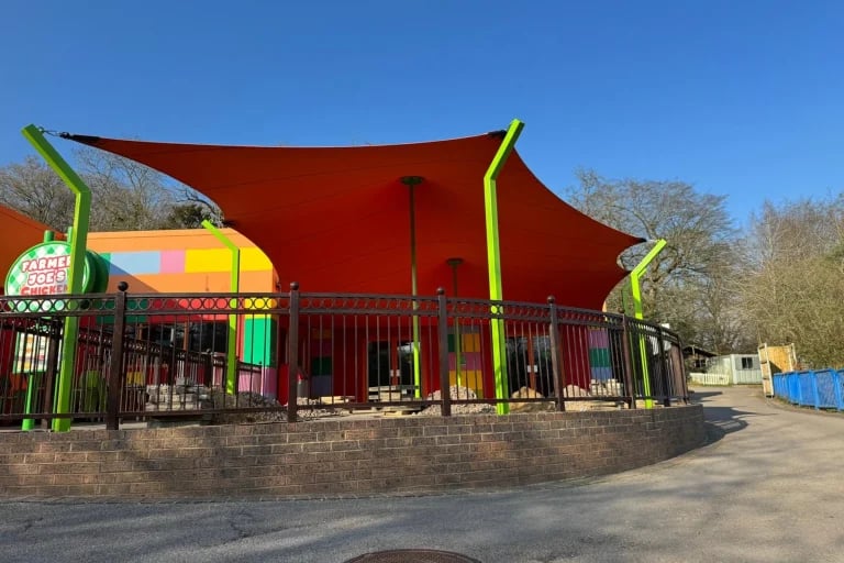 Vista de la entrada principal de una estructura « Carpa Tensada » de RHI, de color naranja brillante y fabricada a medida, que cubre una zona de descanso del parque Legoland.