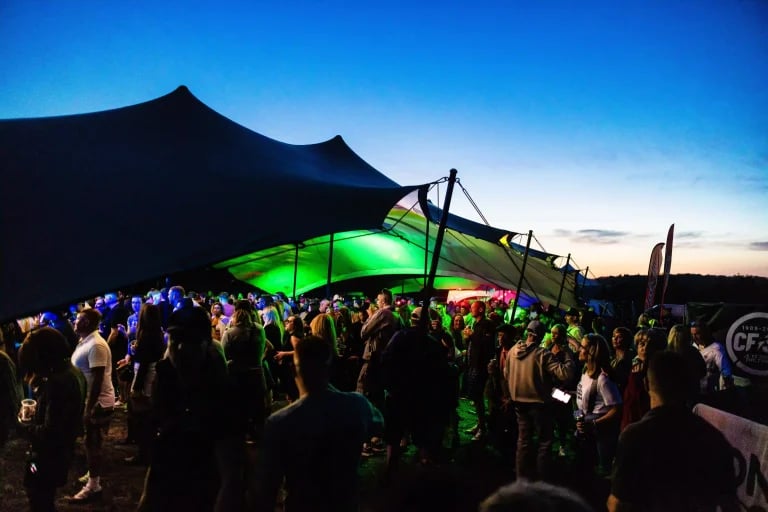 Vue extérieure rapprochée d'un grand abri noir de la marque RHI tente stretch abritant les festivaliers