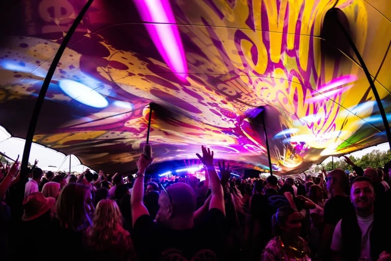 Vue d'une verrière imprimée et éclairée de couleurs, montrant la foule d'un festival sous un grand « RHI » tente stretch avec un éclairage de scène