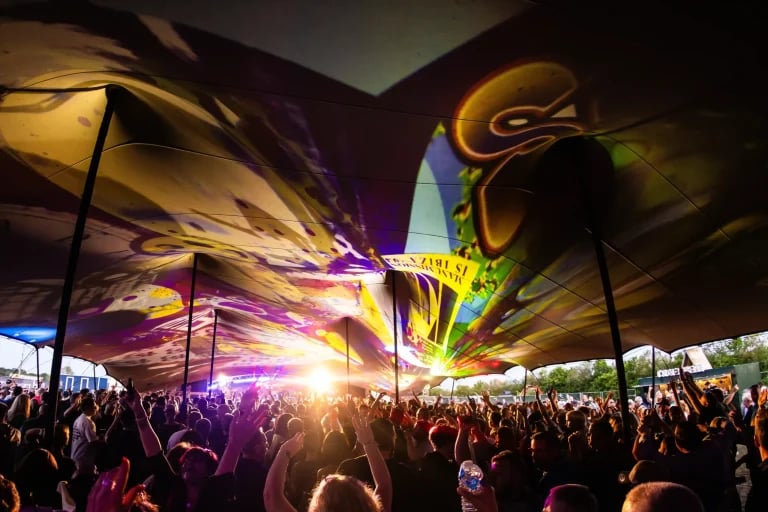 Intérieur d'un chapiteau orné d'une grande impression représentant une foule de festivaliers sous un immense panneau « RHI » tente stretch , avec l'éclairage de la scène