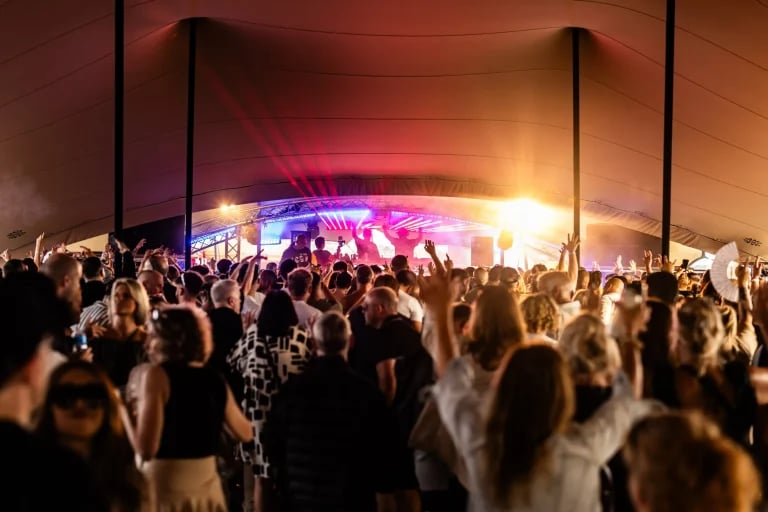 Vue de la foule d'un festival, face à la scène, sous une grande structure « RHI » tente stretch , avec l'éclairage de la scène