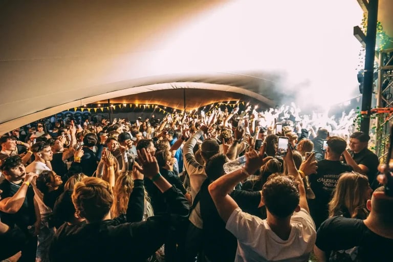Vue d'ensemble d'une foule dense lors d'un festival, sous une grande structure « RHI » tente stretch , avec l'éclairage de la scène