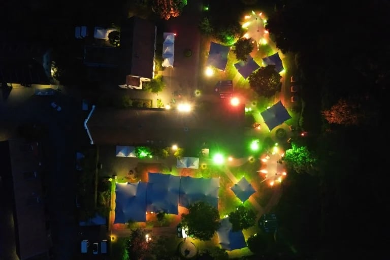 Vue aérienne nocturne d'une fête mettant en scène plusieurs installations « RHI » tentes stretch reliées entre elles sur un vaste site de festival