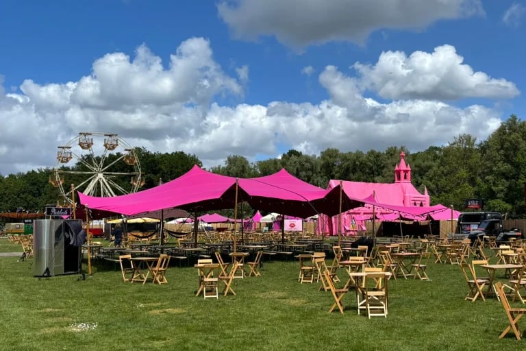 Vue d'ensemble extérieure d'un festival, montrant une tente « RHI » tente stretch de couleur rose vif recouvrant les gradins du festival