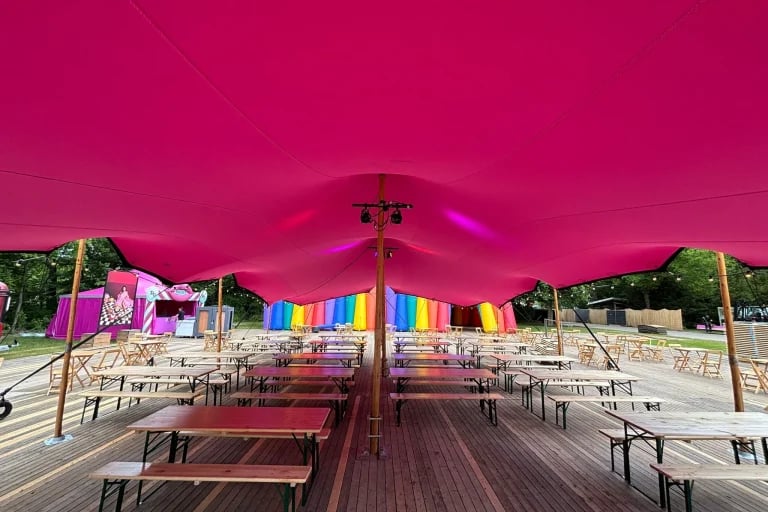 Vue centrale de l'intérieur d'une tente « tente stretch » de RHI, de couleur rose vif, abritant des gradins de festival