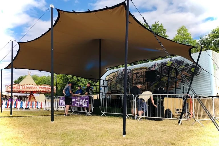 Vue de face, du côté de la scène, d'une structure RHI tente stretch de couleur sombre recouvrant un espace de restauration et de sièges lors d'un festival