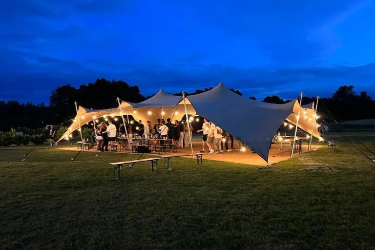 Extérieur nocturne éclairé d'une installation « RHI tente stretch » aménagée dans une cour-jardin paysagée