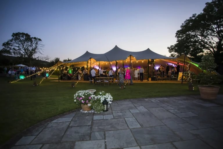 Vue nocturne grand format et éclairée d'un « tente stretch » de RHI aménagé pour une garden-party ou une réception privée