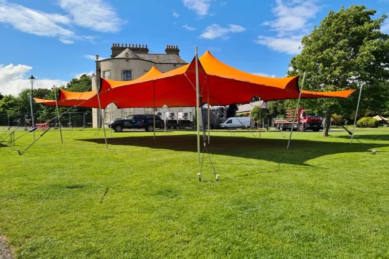 Vue extérieure de face d'une grande installation RHI tente stretch de couleur orange, installée sur une pelouse soignée en Irlande