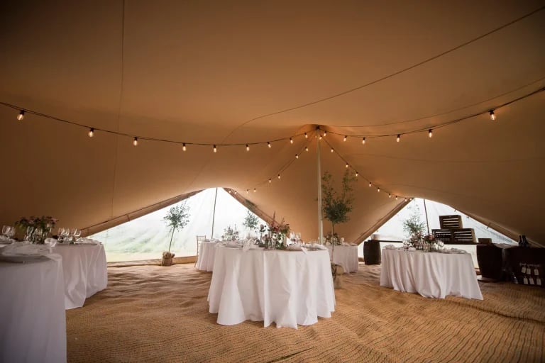 Intérieur de salle de réception ouverte, agrémenté de guirlandes lumineuses issues d'une « RHI » tente stretch , avec cloisons et portes installées, aménagé pour un mariage ou une réception en plein air