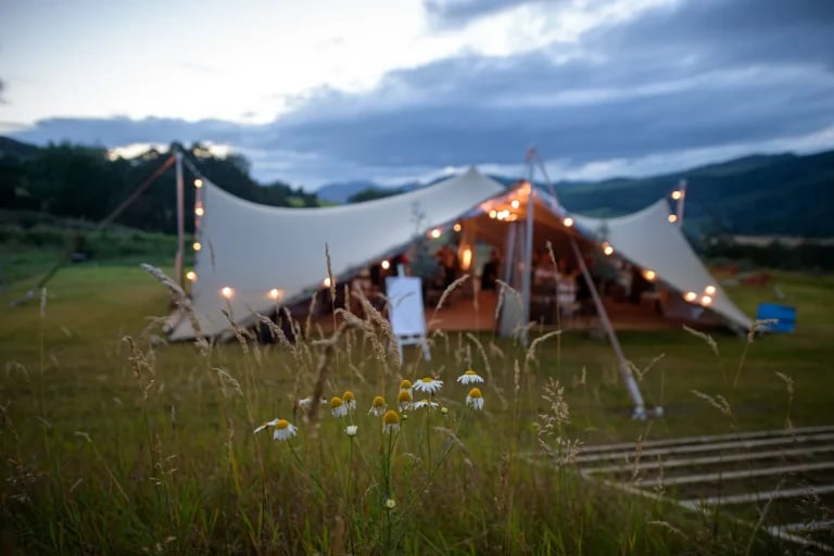 Photo de nuit en extérieur d'un lieu de réception « RHI » ( tente stretch ) au Royaume-Uni, mise en scène pour un mariage ou une réception en plein air, avec une faible profondeur de champ