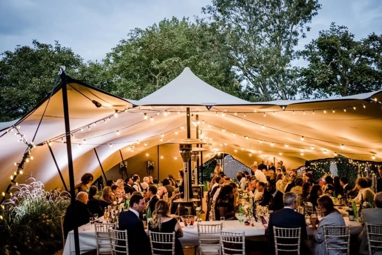 Réception illuminée avec les invités d'une « tente stretch » organisée par RHI au Royaume-Uni, mise en scène pour un mariage ou une réception en plein air