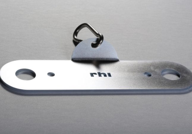 Een plat metalen RHI-bevestigingsgereedschap naast een klein driehoekig metalen hulpstuk en een ring